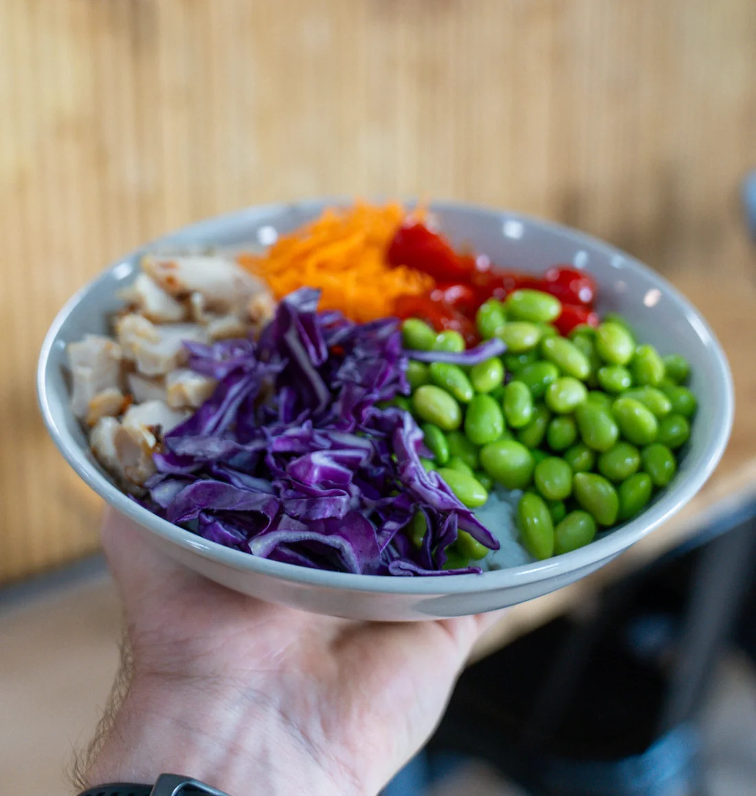 Une salade Pure Taste tenue à la main : poulet, chou rouge, edamame, carottes et tomates